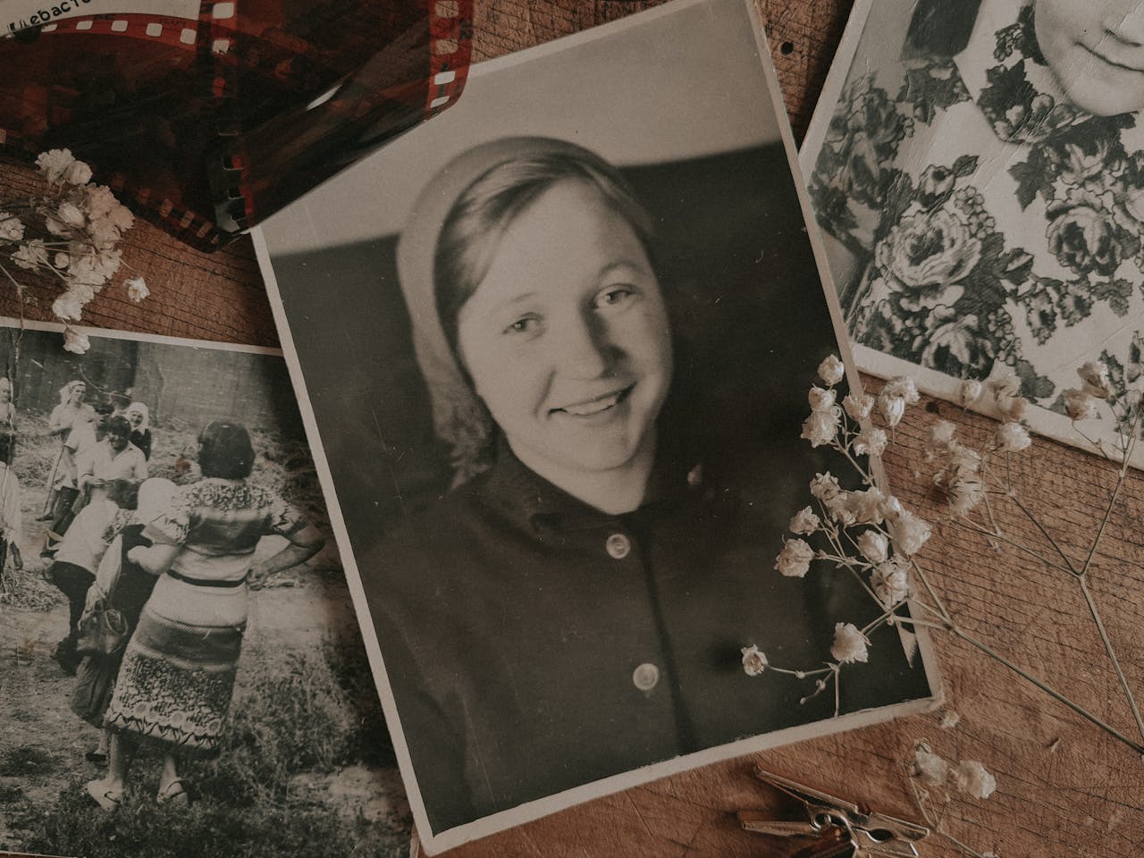 An arrangement of vintage family photos with dried flowers and film negatives, evoking nostalgia.